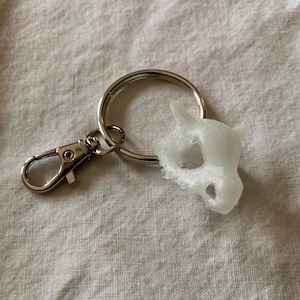 May include: White plastic keychain with a skull-shaped charm attached to a silver key ring.