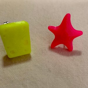 May include: Two 3D printed objects, a yellow rectangle and a pink star, on a white fabric background.