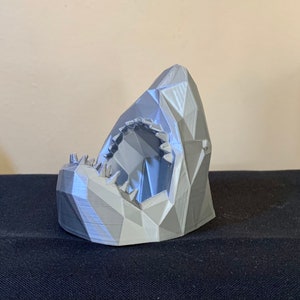 Puede incluir: Una escultura de cabeza de tiburón gris impresa en 3D con un diseño geométrico. La boca del tiburón está abierta, revelando filas de dientes.