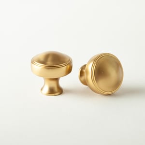 May include: Two gold-colored cabinet knobs with a rounded top and a short, pedestal-like base. One knob is upright, and the other is lying on its side. The knobs have a matte finish and are set against a white background. The text "2 PACK" is in the lower right corner.