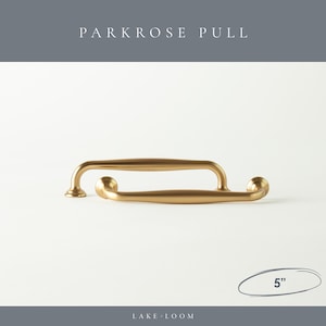 以下が含まれることがあります： 2つのゴールドカラーのParkroseプルハンドル。各約12.7cm。ハンドルは、丸みを帯びた端と中央のバーを備えた湾曲したデザインです。「PARKROSE PULL」の文字が上部に、「LAKE LOOM」の文字が下部にあります。