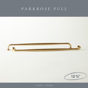 以下が含まれることがあります： ゴールドカラーのParkroseプル2本。各プルは32.07 cmの長さです。プルは、両端に小さな装飾的なディテールを備えた湾曲したデザインです。「PARKROSE PULL」というテキストが画像の上部にあり、「LAKE LOOM」が下部にあります。