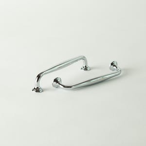 May include: Two polished chrome cabinet pulls. One is a straight bar with curved ends, and the other is a curved bar. Both have decorative, round bases. These hardware pieces are designed for furniture and cabinetry.