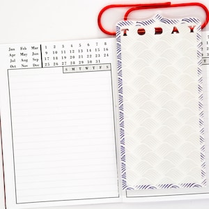 May include: A white planner with a black calendar grid and lined pages. The planner has a clear plastic bookmark with a decorative pattern and the word "TODAY" printed on it.