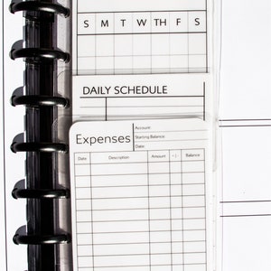 May include: A planner insert with sections for to-do lists, notes, a weekly schedule, and expense tracking. The pages are white with black text and lines, held together by a black binder.