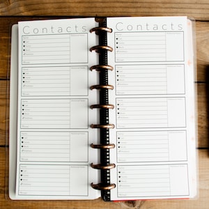 May include: A white, two-page, spiral bound notebook with the word "Contacts" printed at the top of each page. The notebook has lines for writing down names, phone numbers, and addresses.