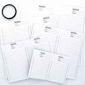 May include: A stack of blank white lined notepads with the word "NOTES" and the words "DATE" and "SUBJECT" printed at the top of each notepad.