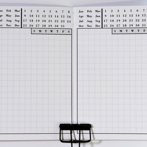 May include: A blank monthly calendar planner with a grid layout. The calendar is divided into two sections, each with a month's worth of dates. The months are labelled January through December. The days of the week are labelled S, M, T, W, T, F, S.