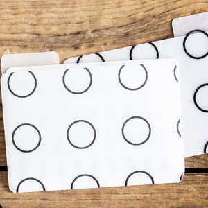 May include: Two white plastic file folders with black circle patterns. The folders are stacked on top of each other.
