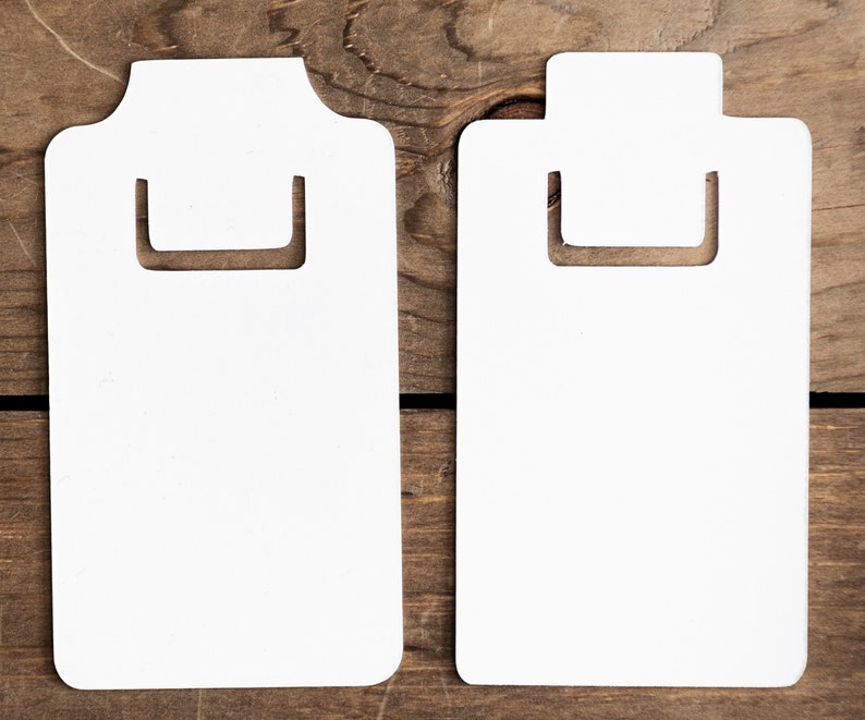 May include: Two white cardboard clipboard style tags with a cut-out handle. The tags are blank and ready to be written on.