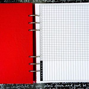 May include: A white page with a grid pattern and numbers 1 through 31 listed down the left side. The page is labeled "JANUARY" at the bottom. The page is part of a red binder.