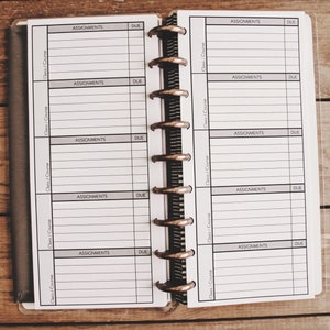 May include: A black and white planner with a clear plastic cover. The planner has a ring binding and is divided into two sections. Each section has five columns labeled "Class/Course", "Assignments", and "Due".