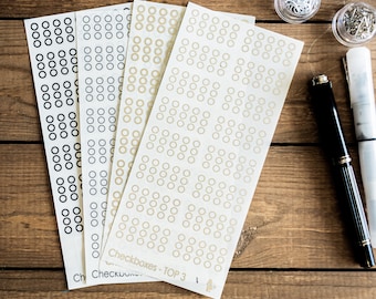Op de afbeelding: Drie vellen papier met rijen cirkels. De cirkels zijn zwart, wit en beige. De tekst "Checkboxes - TOP 3" staat onderaan de vellen.