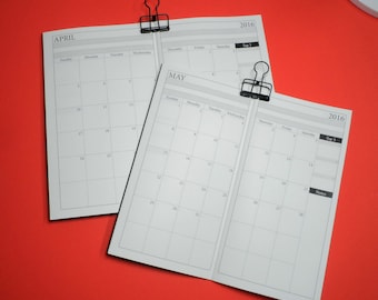 May include: Two open 2016 monthly calendar pages, April and May, held together with black binder clips. The calendars are white with gray grid lines and text. The background is a solid red-orange color.