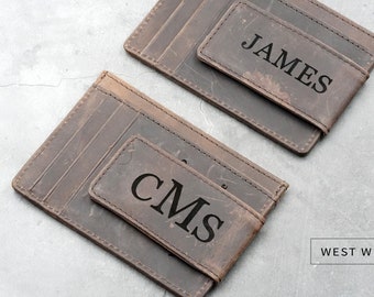 May include: Two brown leather wallets with a money clip. One wallet is personalized with the name "JAMES" and the other with the initials "CMS". The wallets are made by West Wind Co.