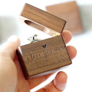 Peut inclure: Une bo&icirc;te &agrave; bague en bois avec un c&oelig;ur et l'inscription "i love you more". La bo&icirc;te est ouverte et une bague en argent se trouve &agrave; l'int&eacute;rieur.