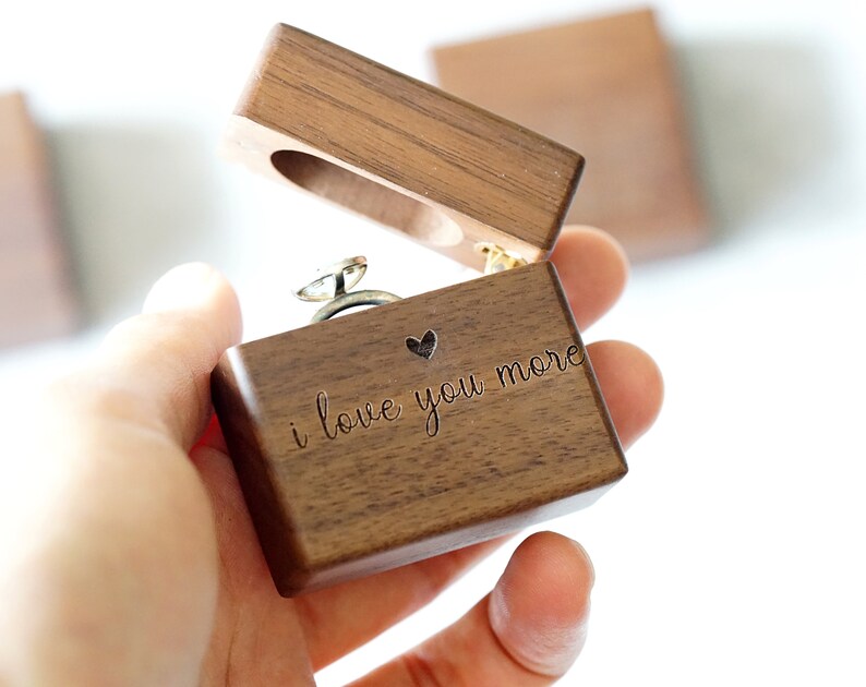 Peut inclure: Une bo&icirc;te &agrave; bague en bois avec un c&oelig;ur et l'inscription "i love you more". La bo&icirc;te est ouverte et une bague en argent se trouve &agrave; l'int&eacute;rieur.