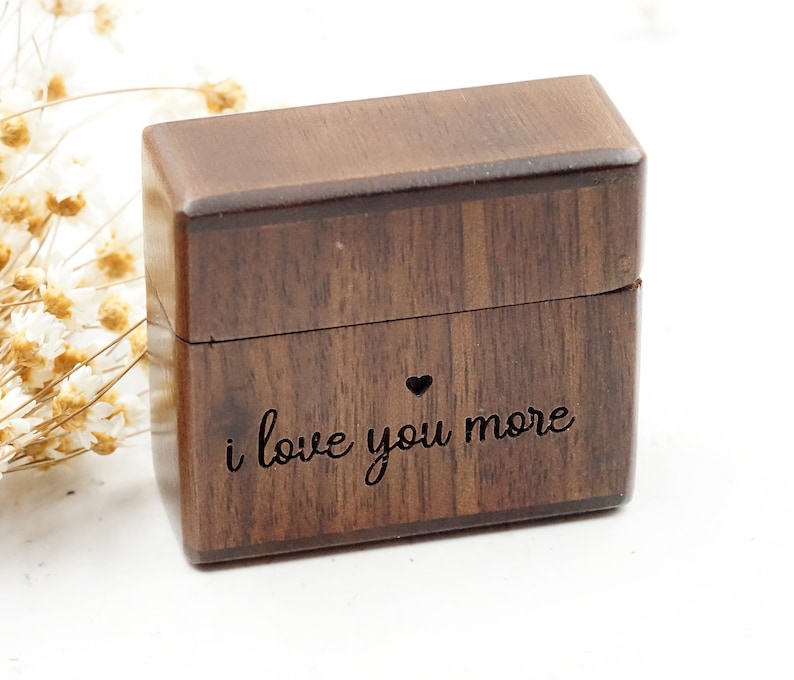 Peut inclure: Une petite bo&icirc;te en bois avec un couvercle &agrave; charni&egrave;re. La bo&icirc;te est de couleur brun fonc&eacute; et porte les mots "i love you more" grav&eacute;s sur le devant, ainsi qu'un petit c&oelig;ur.