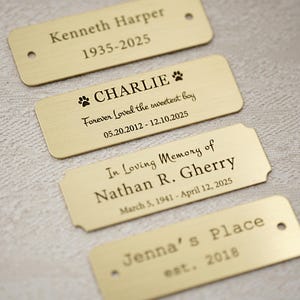 May include: Four rectangular brass nameplates with engraved text. The plates include names, dates, and phrases like "Forever Loved the sweetest boy" and "In Loving Memory of." One plate is for "Jenna's Place, est. 2018."
