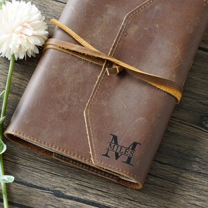 May include: Brown leather journal with a tan leather strap and a personalised monogram that reads "M MILES".