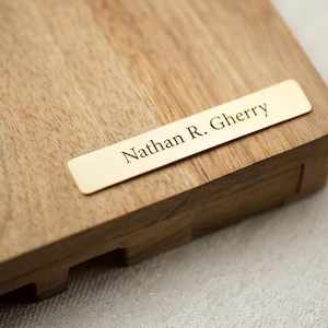 May include: A wooden box with a brass nameplate bearing the name "Nathan R. Gherry". The box is made of light-coloured wood, and the nameplate is rectangular. The text is in a serif font.