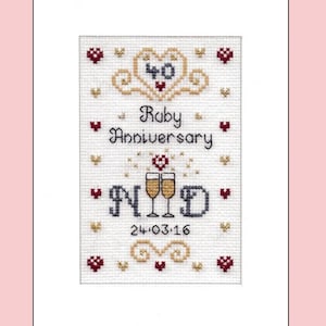 May include: Cross-stitch design on white fabric, framed in a white border. The artwork features the words "Ruby Anniversary" and "NYD" with champagne glasses. Includes the number "40" and the date "24.03.16". Decorated with hearts and other decorative elements.