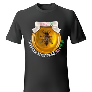 May include: Black t-shirt featuring a graphic of a bee inside a honey jar with the text "HONEY DO". The text "THE WOMAN OF MY HEART WEARS PINK & GREEN" is also printed on the shirt.