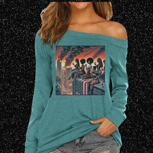 May include: Teal off-the-shoulder long-sleeve shirt with a graphic print of women on a rooftop overlooking a city skyline. The shirt has the text "A NEW MERCH" and "A NEW ATTITUDE @ 92%."