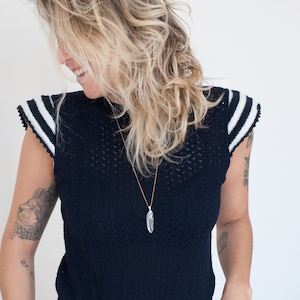 May include: A woman wearing a dark blue knitted top with white stripes on the sleeves and a crystal pendant necklace.