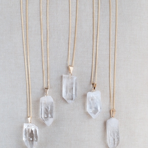 May include: Five gold chain necklaces with clear quartz crystal pendants. The pendants are all different shapes and sizes.