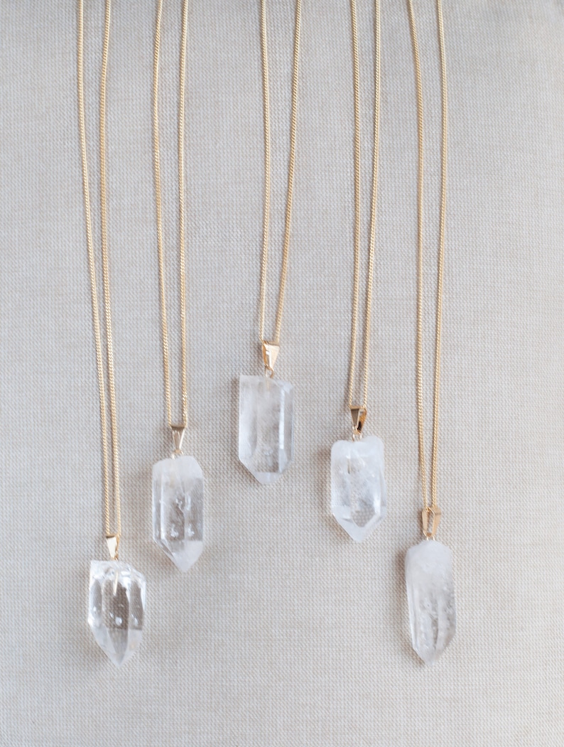 May include: Five gold chain necklaces with clear quartz crystal pendants. The pendants are all different shapes and sizes.