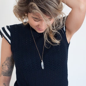May include: A person wearing a dark blue knitted top with white stripes on the sleeves and a crystal pendant necklace.
