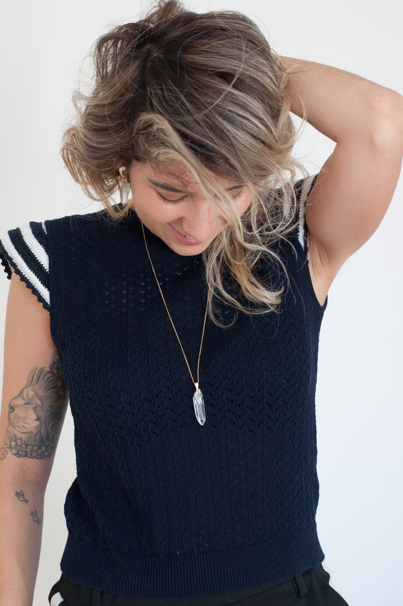 May include: A person wearing a dark blue knitted top with white stripes on the sleeves and a crystal pendant necklace.