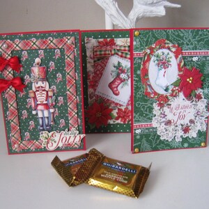 May include: A festive Christmas card set with a green and red plaid design, featuring a nutcracker, poinsettias, and a stocking. The cards are accompanied by two Ghirardelli chocolate bars.