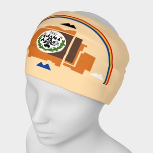 May include: A beige headband featuring a colorful design. The design includes a state seal, geometric shapes in shades of brown and orange, and a rainbow arc. The headband is worn on a mannequin head.