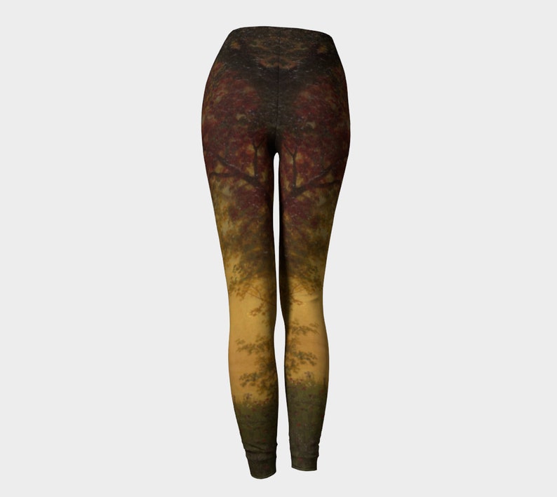 May include: A pair of leggings featuring a colourful autumnal forest scene printed on them. The leggings are a dark brown colour with a gradient of yellow and green at the bottom.