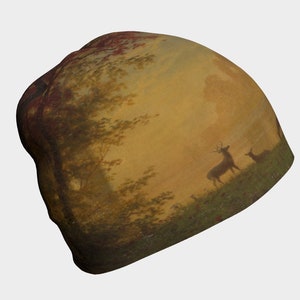 May include: A brown and beige beanie featuring a painting of a woodland scene with two deer in the foreground. The sky is a pale yellow with a touch of orange.