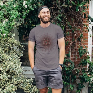 以下が含まれることがあります： 赤い、緑色、黄色のマンダラ模様の入ったチャコールグレーのTシャツを着た男性。Tシャツは半袖でクルーネックです。