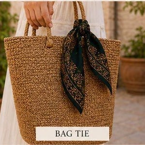 May include: A woven brown tote bag with rope handles. A dark green scarf with a gold pattern is tied to one of the handles. The text "BAG TIE" is displayed on a white rectangle at the bottom of the bag.