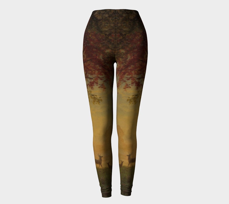 May include: A pair of leggings featuring a printed forest scene. The design includes a sunset, trees, and deer. The leggings are a gradient of red, orange, and yellow.