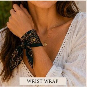 May include: A dark green wrist wrap with a gold paisley design is tied around a wrist. A gold necklace with a pendant is also visible. The text "WRIST WRAP" is displayed in a white rectangle at the bottom of the image.