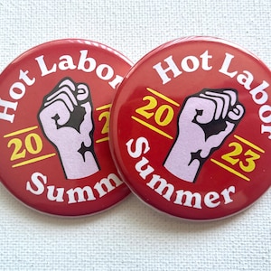 May include: Two red round buttons with white text that reads "Hot Labor Summer 2023". Each button features a stylized fist with a black outline and a pink fill.