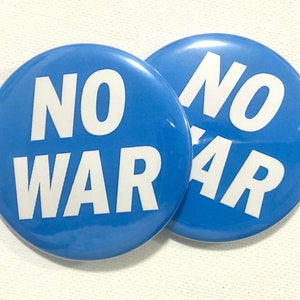 Op de afbeelding: Twee blauwe ronde knoppen met witte tekst die "NO WAR" zegt.