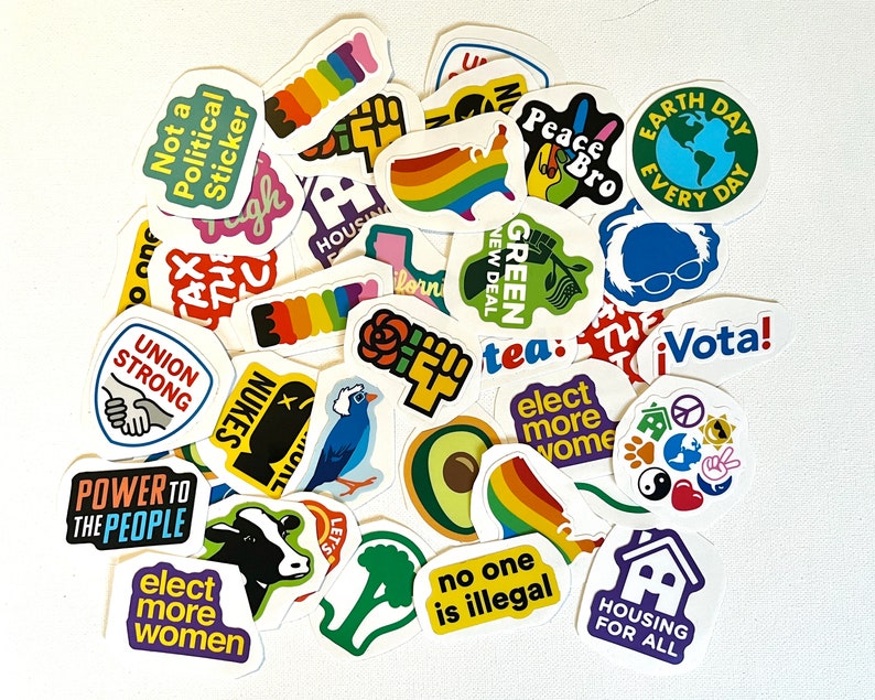 May include: A collection of colorful stickers with various messages and designs, including "Not a Political Sticker", "Union Strong", "Power to the People", "Elect More Women", "Green New Deal", "Earth Day Every Day", "Housing for All", "No One is Illegal", "Vota!" and "Let's Go!"