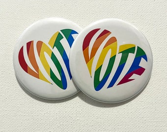 May include: Two white round buttons with a rainbow heart design. The heart is made up of the word "VOTE" in rainbow colors.