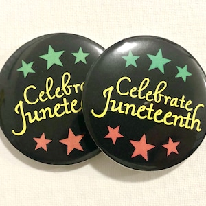 May include: Two black button pins with the text "Celebrate Juneteenth" in yellow lettering. The pins have green and red stars around the text.