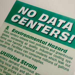 May include: A green and white sign with the text "NO DATA CENTERS!" The sign also includes the text "Environmental Hazard" and "Utilities Strain", along with descriptions of the environmental impact of data centers.