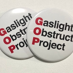 May include: Two white round buttons with the text "GOP Gaslight Obstruct Project" in black and red letters. The letters "GOP" are in red.
