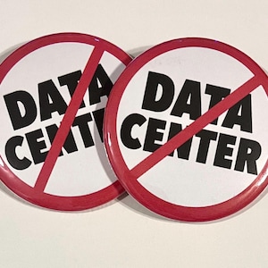 May include: Two round white buttons with a red border and a red diagonal line through the words "DATA CENTER" in bold black letters. The buttons are likely for a protest or awareness campaign.