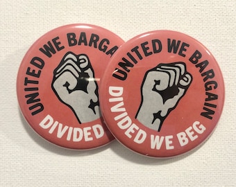 May include: Two pink button badges with a black fist and white text. The text on the badges reads "United We Bargain, Divided We Beg".